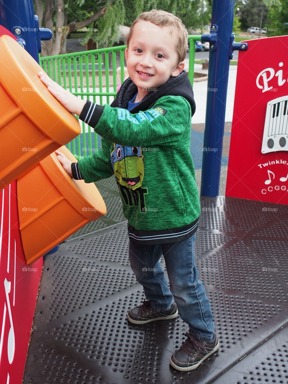 A little boy enthusiastically plays on the plastic drums on a play structure in the park. 