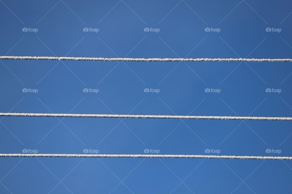 Electric wires covered with snow against the blue sky 