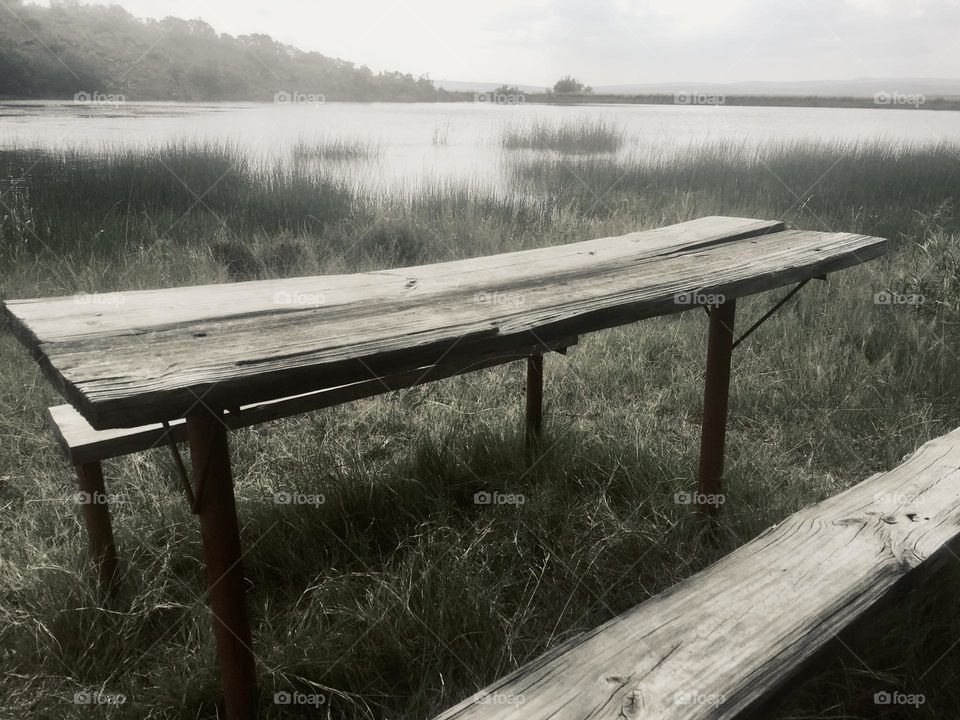 Old wooden weathered table in nature next to a small dam. 