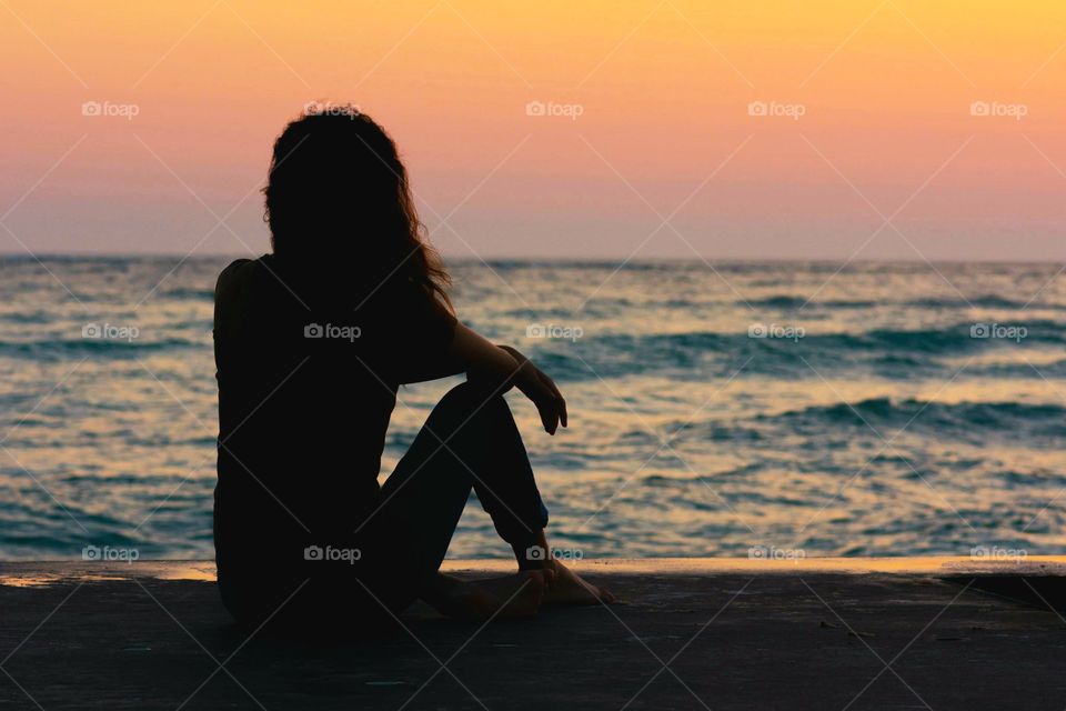 silhouette of a woman enjoying a peaceful evening moment on the beach watching the beautiful pink and orange sunset over the sparkling blue water