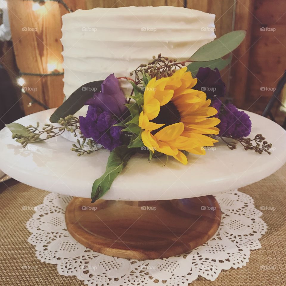 A white frosted wedding cake, decorated by the combination of purple and yellow flowers. 