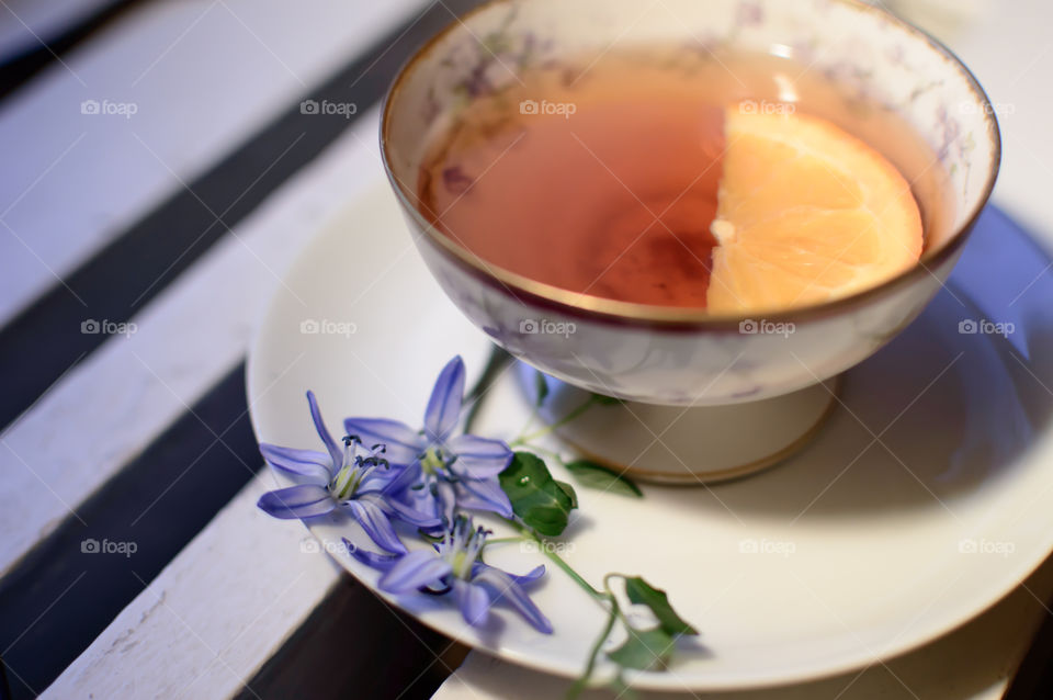 Vintage cup of tea with fresh Scilla siberica lily  garden flowers on white painted wood table and slice of orange fruit tranquil relaxation photography 