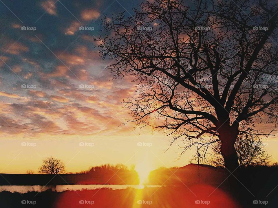 sun setting below horizon and sun rays reflecting on pond in country field