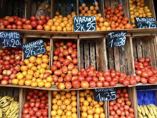 Fresh colorful red yellow orange organic assorted fruits displayed on a market stand inside wooden boxes with Spanish language price tags 