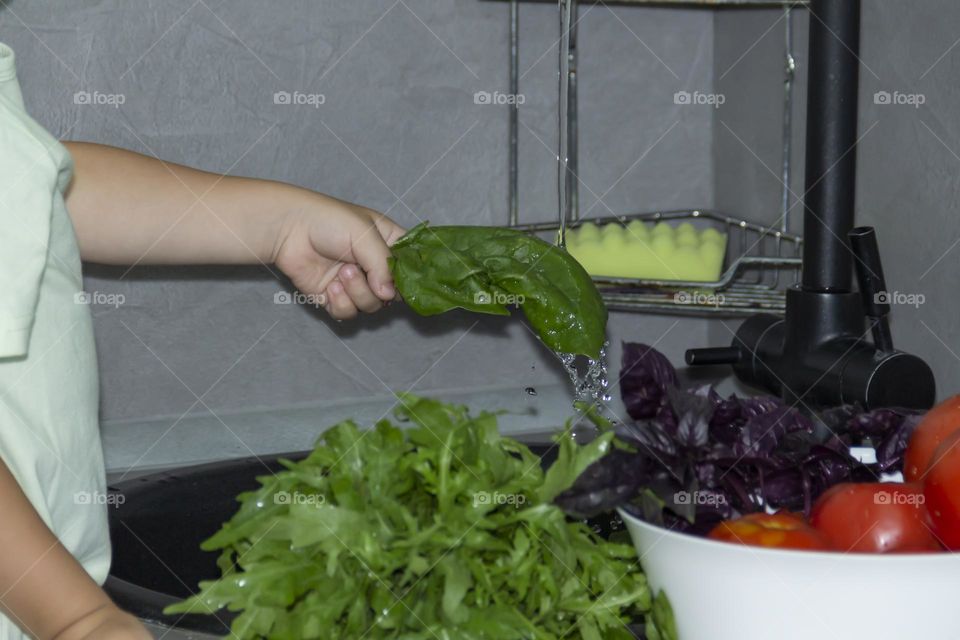 A small child washes spinach under running tap water.