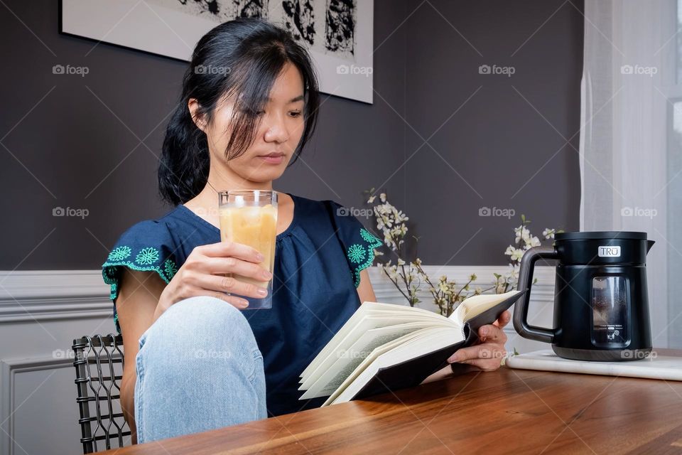 A young lady of Taiwanese decent has a calm moment to enjoy her book with a glass of cold brew. 