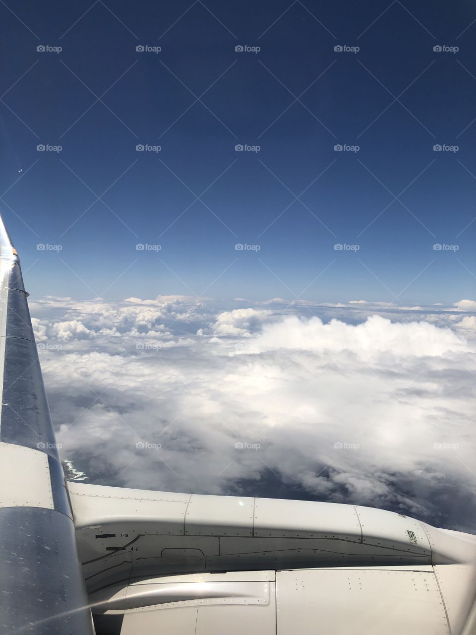 The gorgeous view of clouds, white and fluffy, framed by the wing of an airplane High in the sky. 