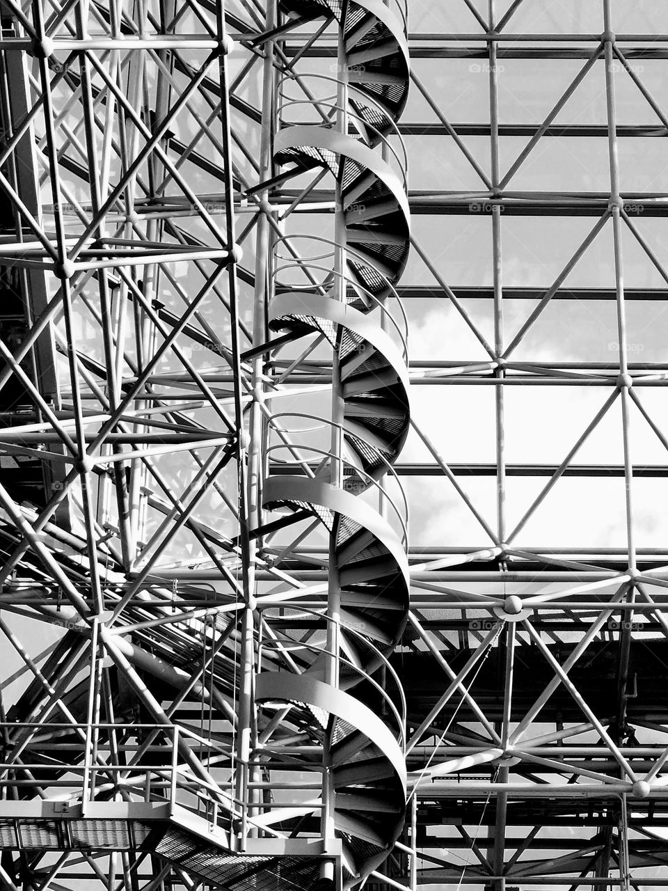 A complex web of geometric angles and steel support a spiral staircase leading to a rooftop