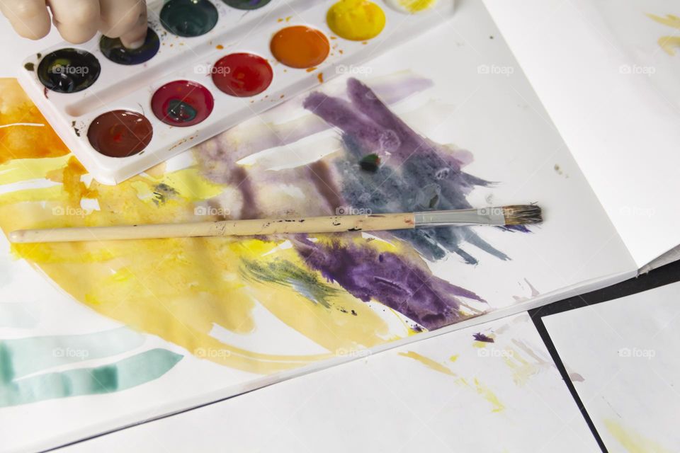 A small child draws with watercolors, multi-colored paints in an album at the table.