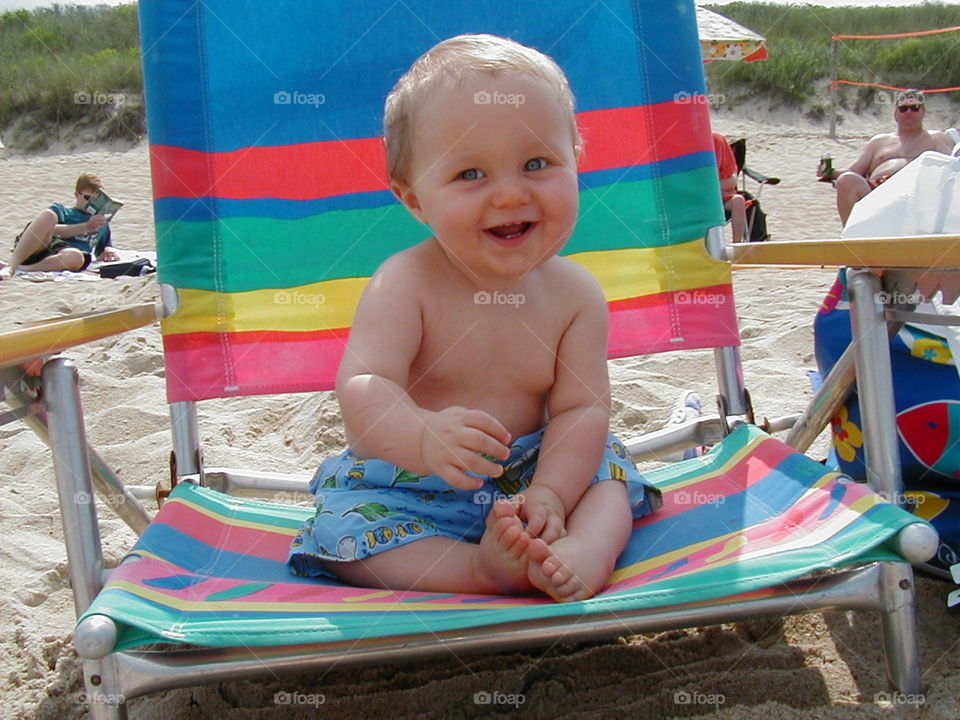 Baby at the beach. A young child sits happily on a beach chair. 