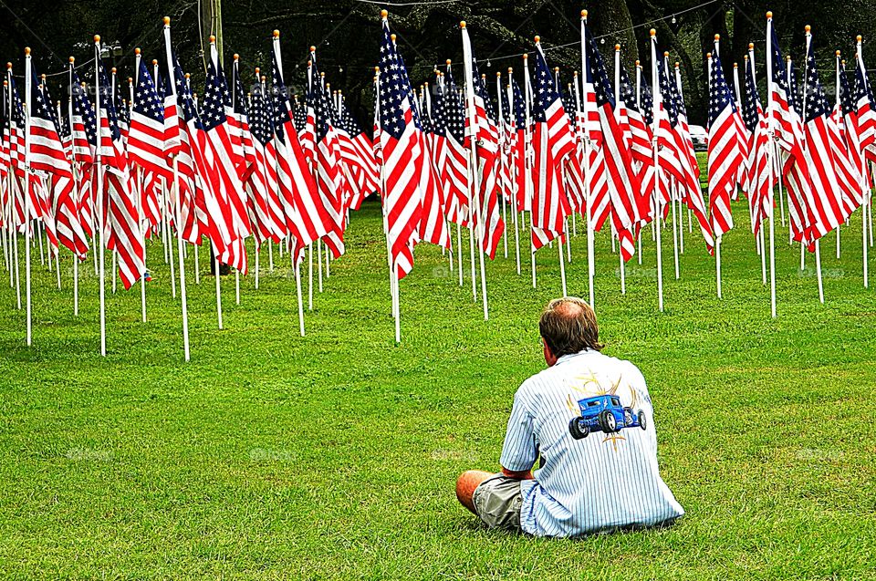 Patriotic Response- A man sits crossed legged facing the display of American Flag 