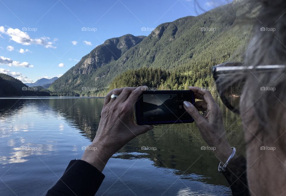 Woman capturing photo of beautiful Canadian mountain lake and reflections 