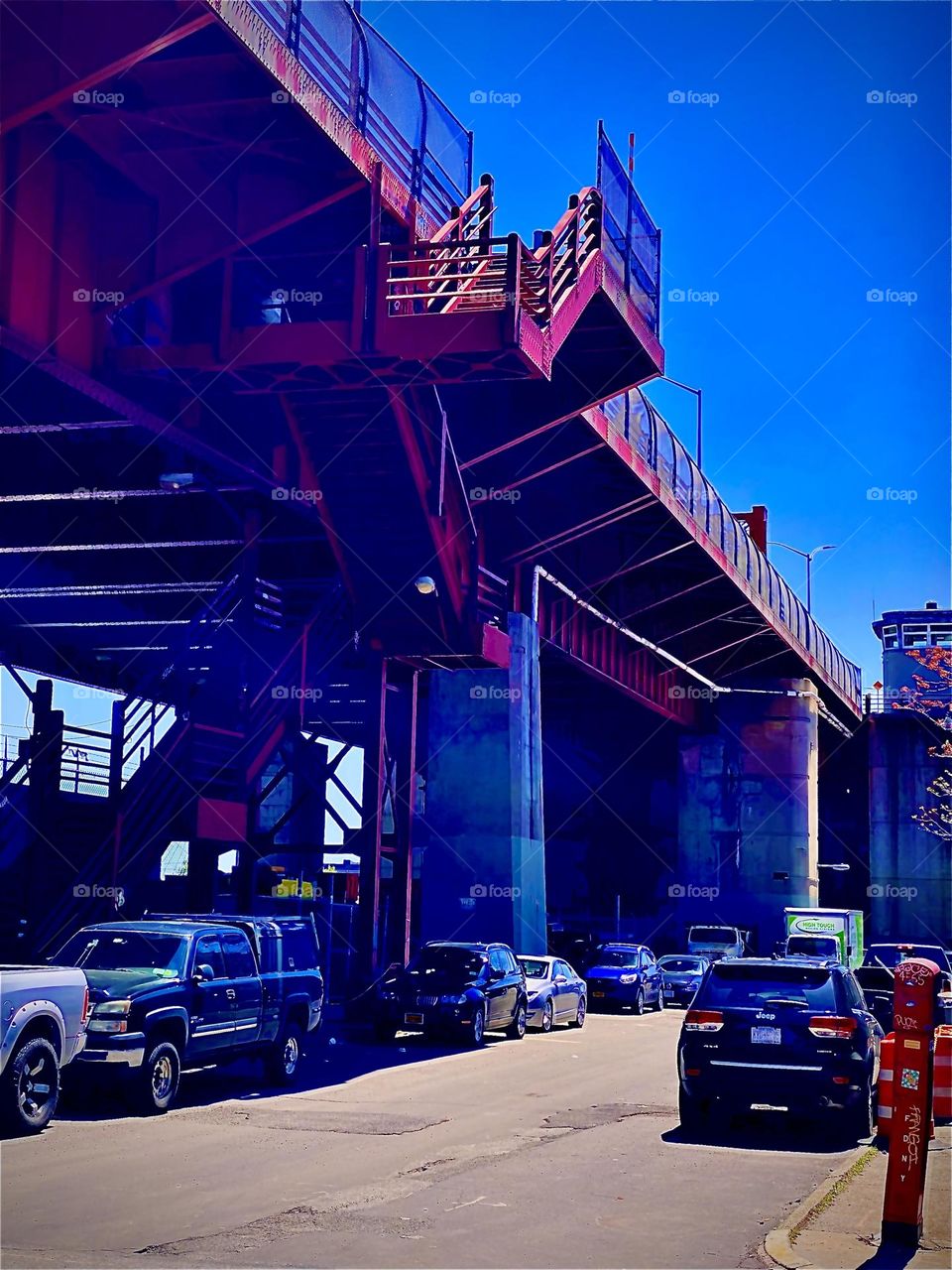 This red metal staircase located in the parking lot beneath the „Pulaski Bridge“ leads up to the pedestrian walkway across the bridge that connects LIC, Queens and Greenpoint, Bklyn, NY. 2022. Hypnotic Productions