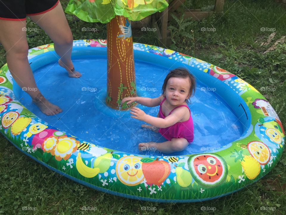 Little girl playing in an inflatable rubber swimming pool outdoors