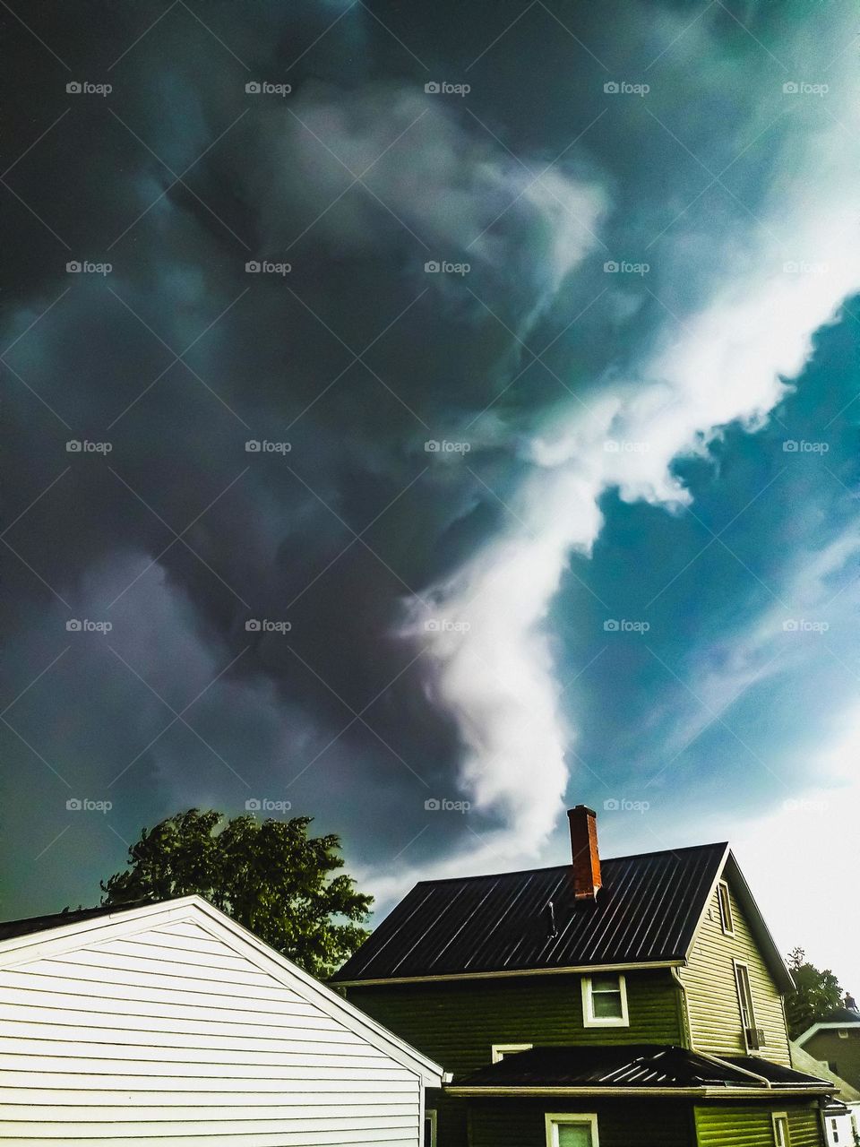 The sky is looming with a Funnel cloud hanging over head and over a neighbors house 