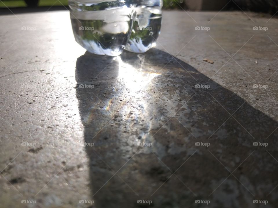 Slight refractions of light creating small rainbows in the shadow of a water bottle.