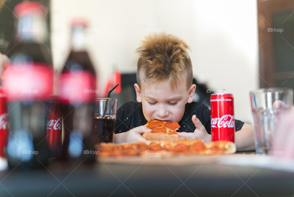 cute boy of seven years old, eats delicious pizza and drinks coca-cola, boy at home