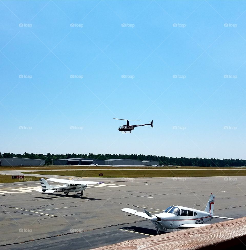 Airport for small planes, helicopter flying. Hangers, runways, blue sky, 2 small planes.