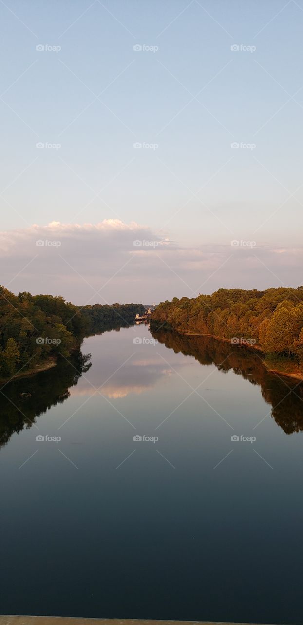 Fall trees surrounding river that reflects the clouds in the sky