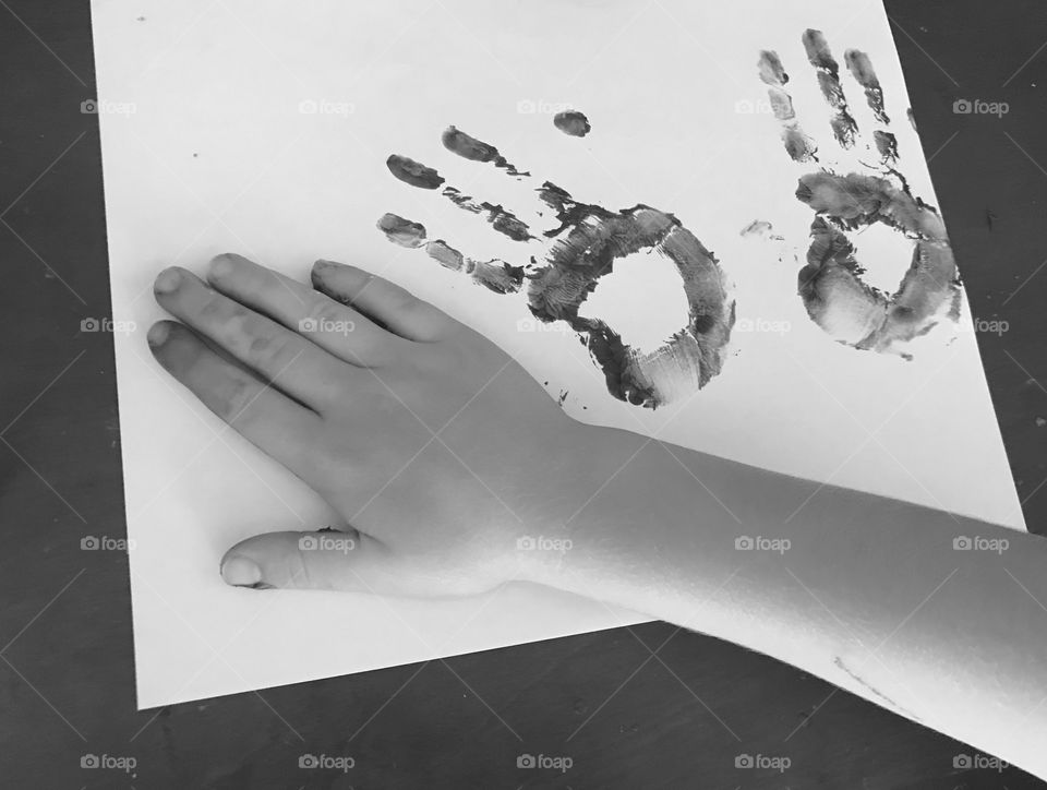 Black and white photo of a little child’s hand prints on a white sheet of paper- child is creating art work 