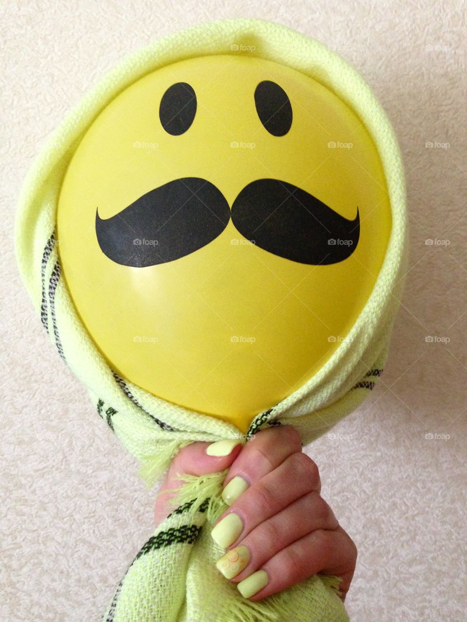 A hand with lemon color nails holding a ballon with funny smile 