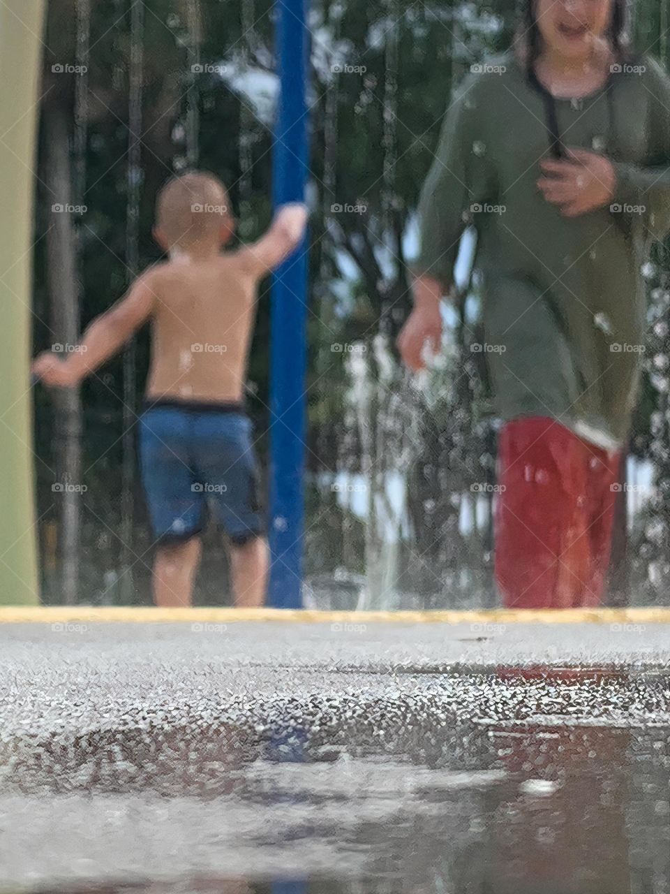 Children having lots of fun in the water at the colorful kids splash pad at the city park for children during a really warm day in Florida.