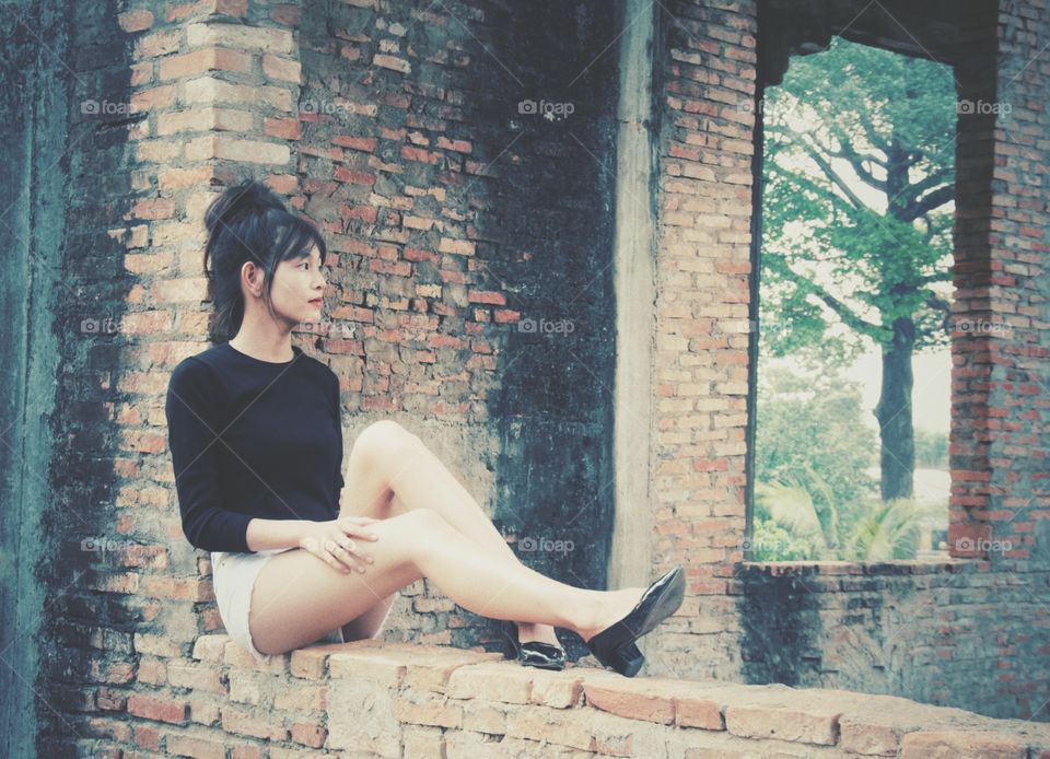 Stylish Asian girl sitting on brick wall