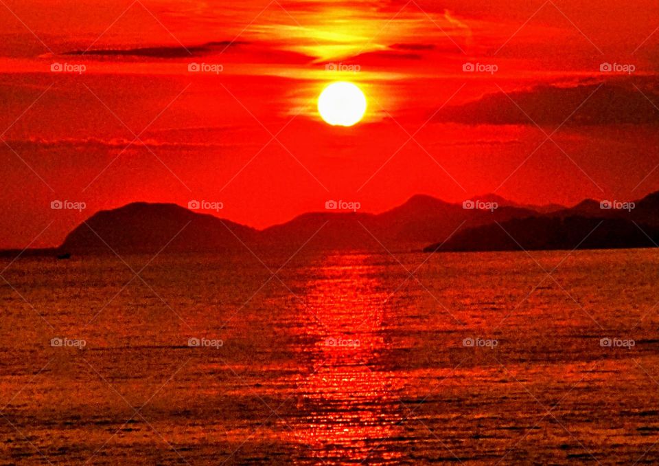 Bright red sunset across the bay of Dubrovnik with glowing yellow sun against the red creating a reflection across the sea