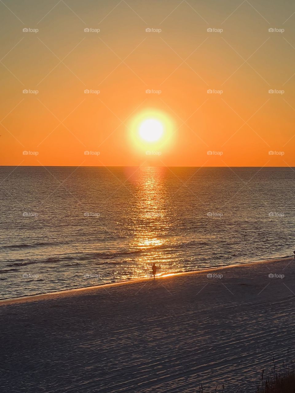 A single person in silhouette on a beach at sunset. The setting sun is a spotlight on the person.