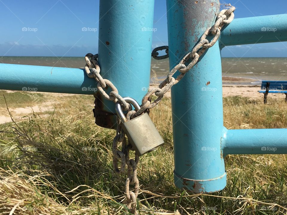 A grey padlock on a teal Aqua marine blue metal gate ocean background 