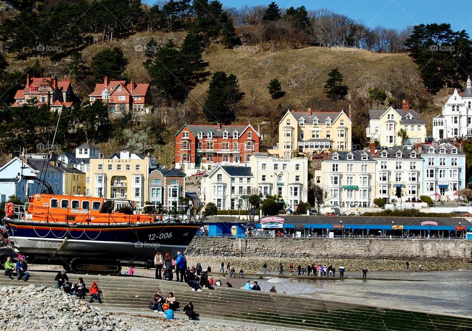 Lifeboat stationed on beach at Llandudno, north Wales, showing low tide and buildings in the background. 