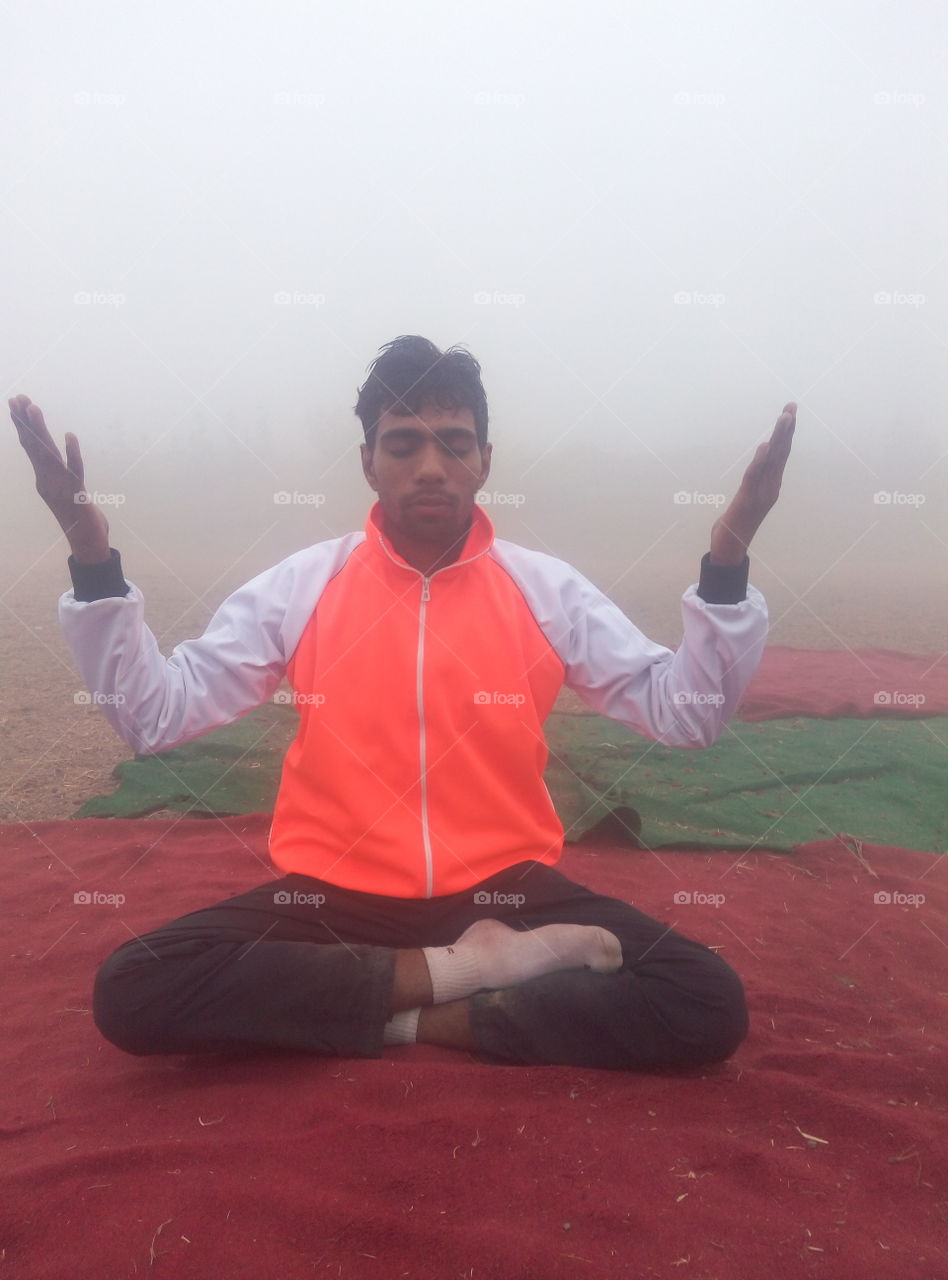 A young man doing yoga on early foggy day