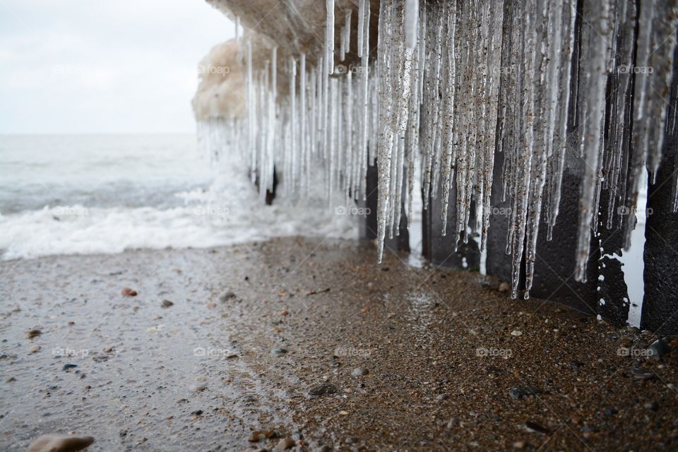 sandy icicles at the beach by the water and waves in winter