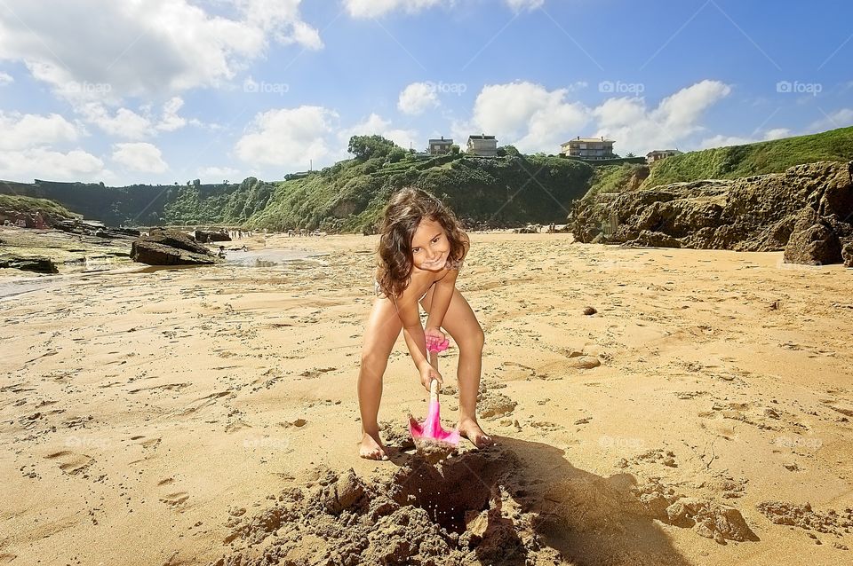 A little girl plays with her toy shovel on the beach in summer