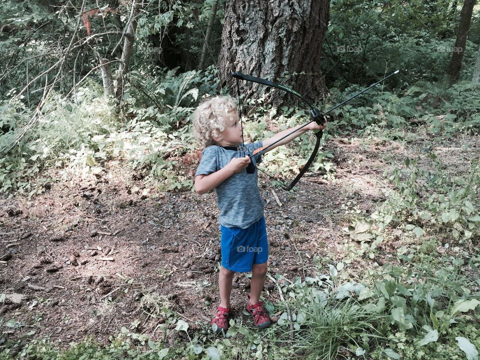 Little boy shooting bow . A little boy stands in the woods shooting a bow and arrow