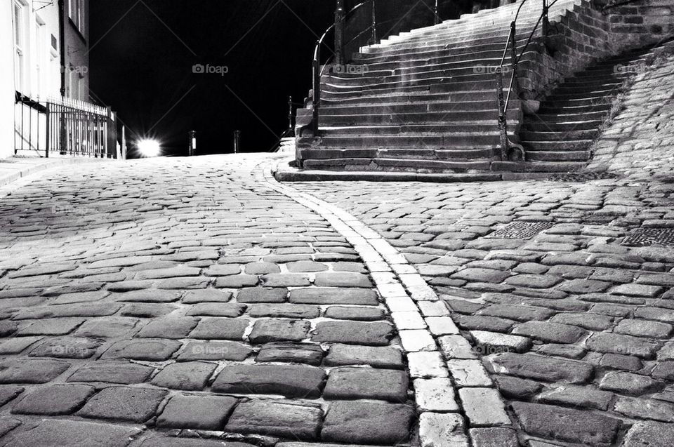 Black and white low angle shot of a cobbled street with steps sweeping