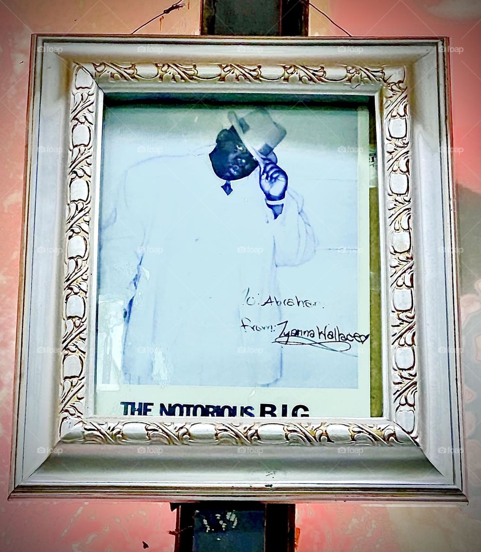 The portrait of the king of „gangsta rap“ behind glass and adorned with a beautiful ornamented golden frame is displayed at KEYFOOD on „Fulton St“. „T‘yanna Wallace“, his daughter hand signed it. 2022. Hypnotic Productions