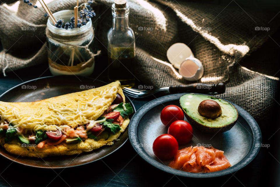 fresh, fluffy omelette with salmon, tomatoes, avocado, cheese and rucola, on a wooden rustic table