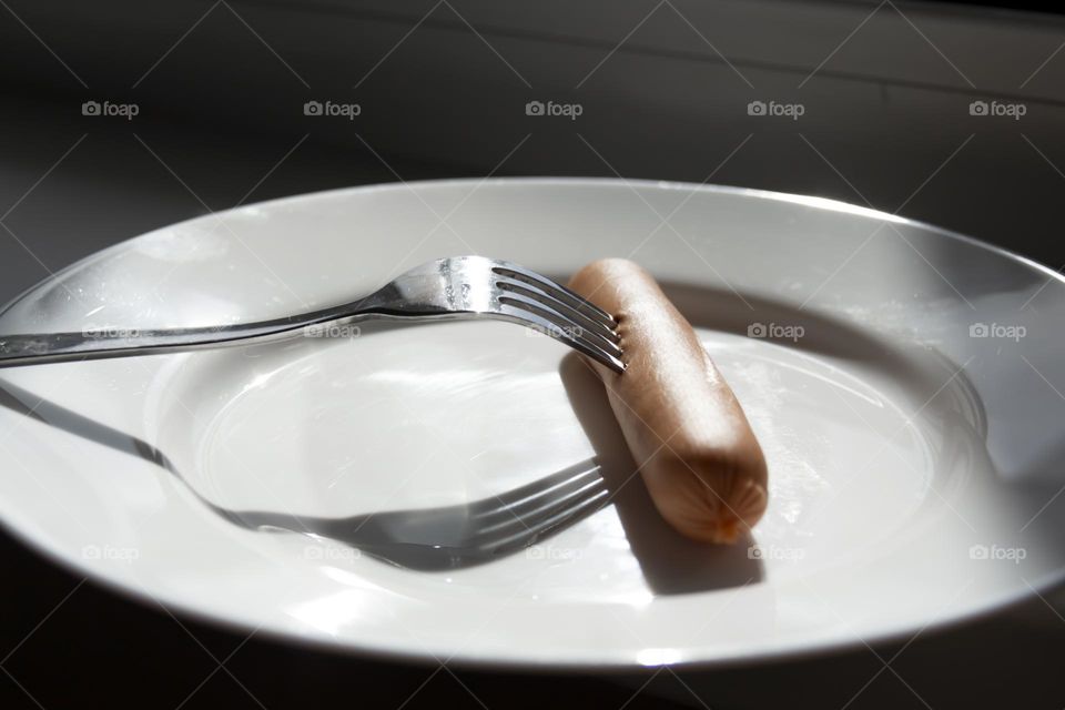 A fork strings a sausage on a white porcelain plate.