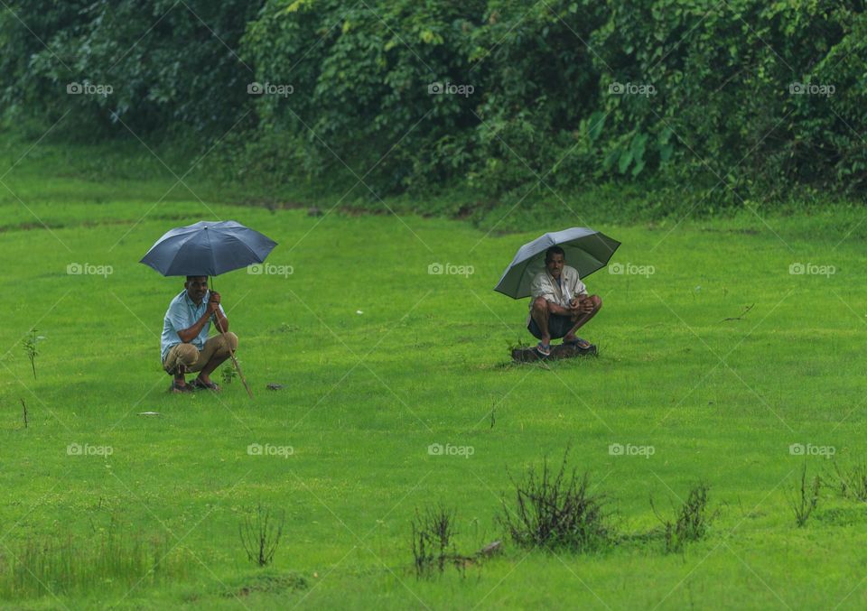 men sitting on the field holding umbrella at countryside