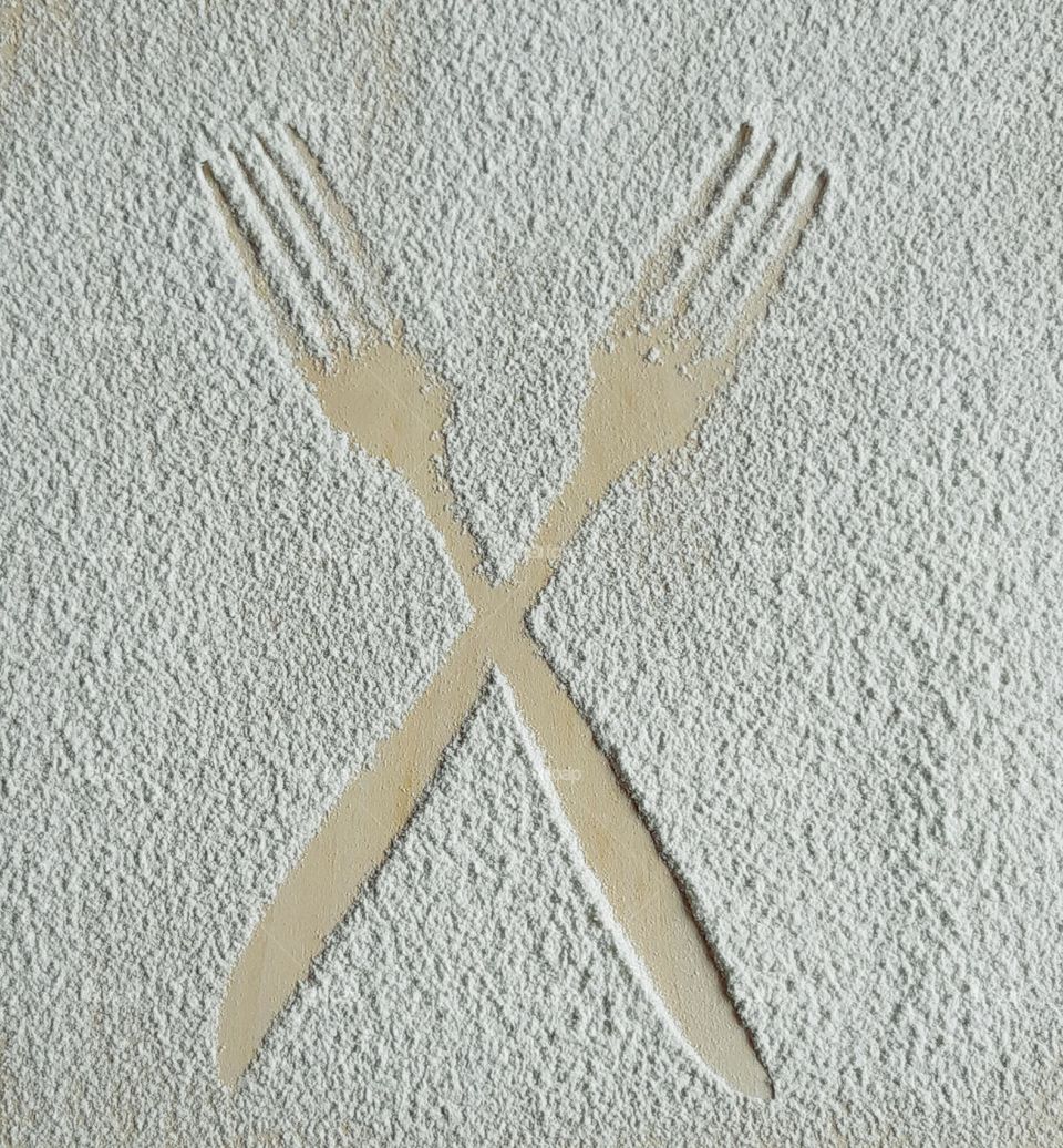 Silhouette of two forks crossed drawing with white flour on wooden background