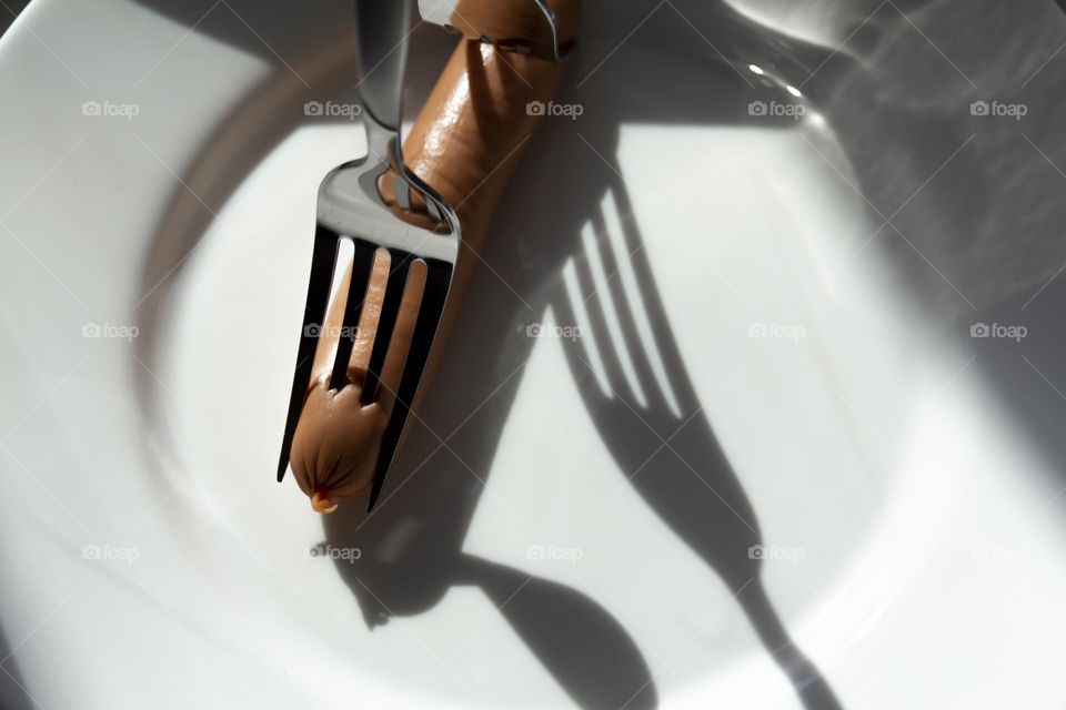 Two forks prick one sausage on a white porcelain plate.