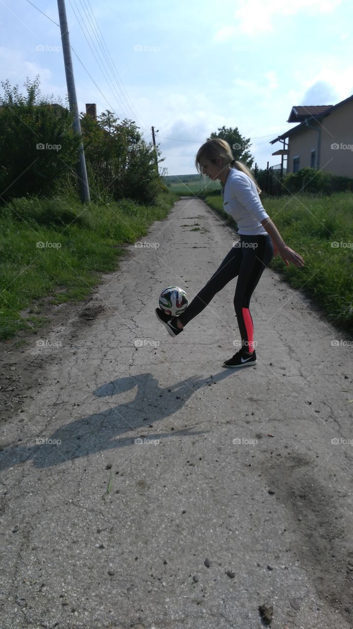 Teenage girl playing football on empty street