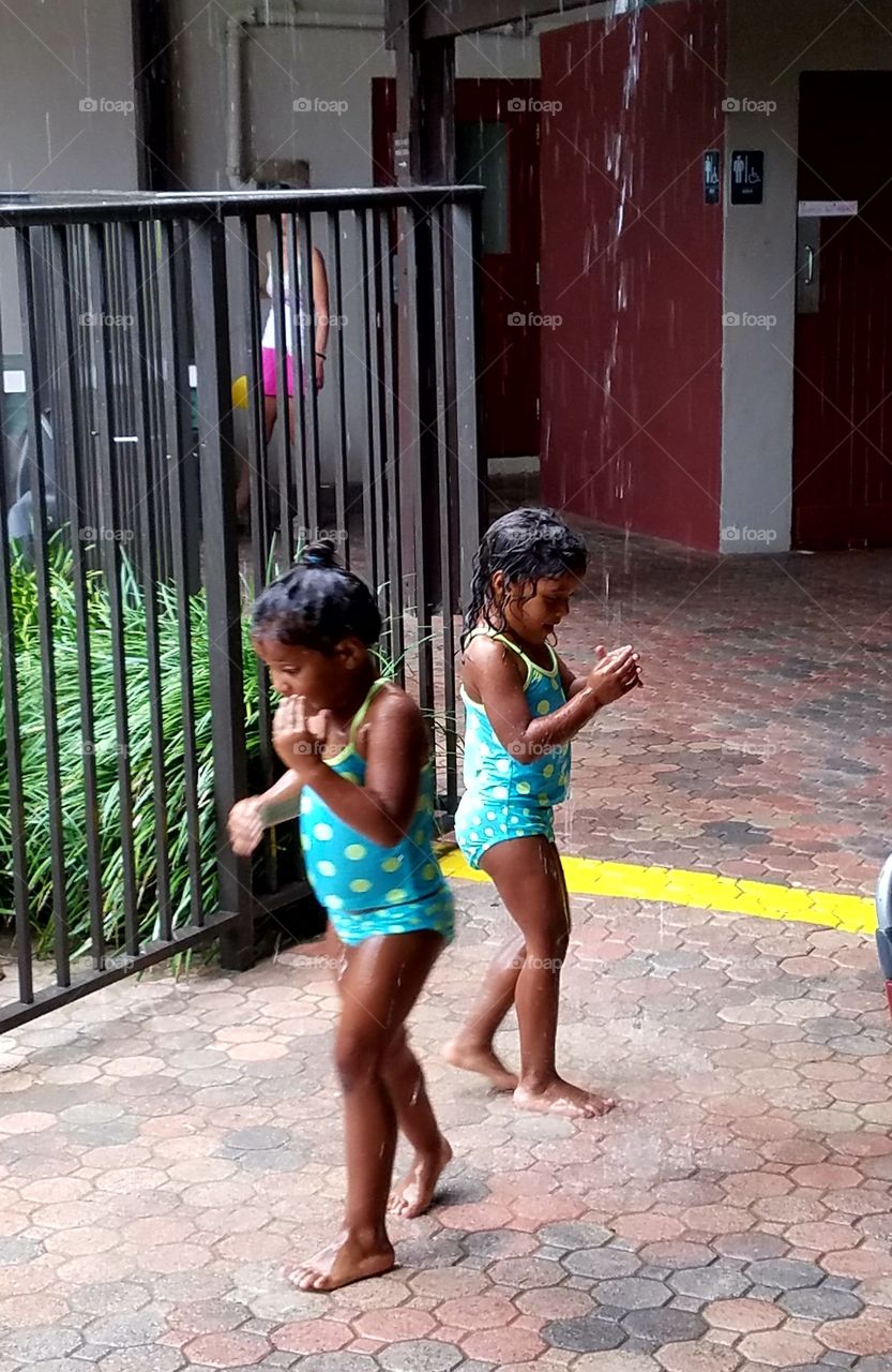 Children playing & splashing in rainwater downspout, puddles, laughing & giggling together. They were little girl twins in cute matching bathing suits.