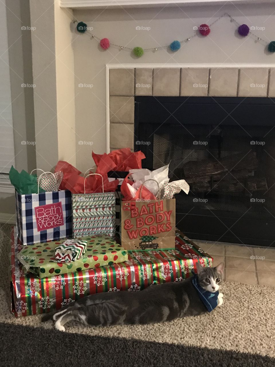 A cute kitten stretched out by a pile of beautifully wrapped Christmas gifts.