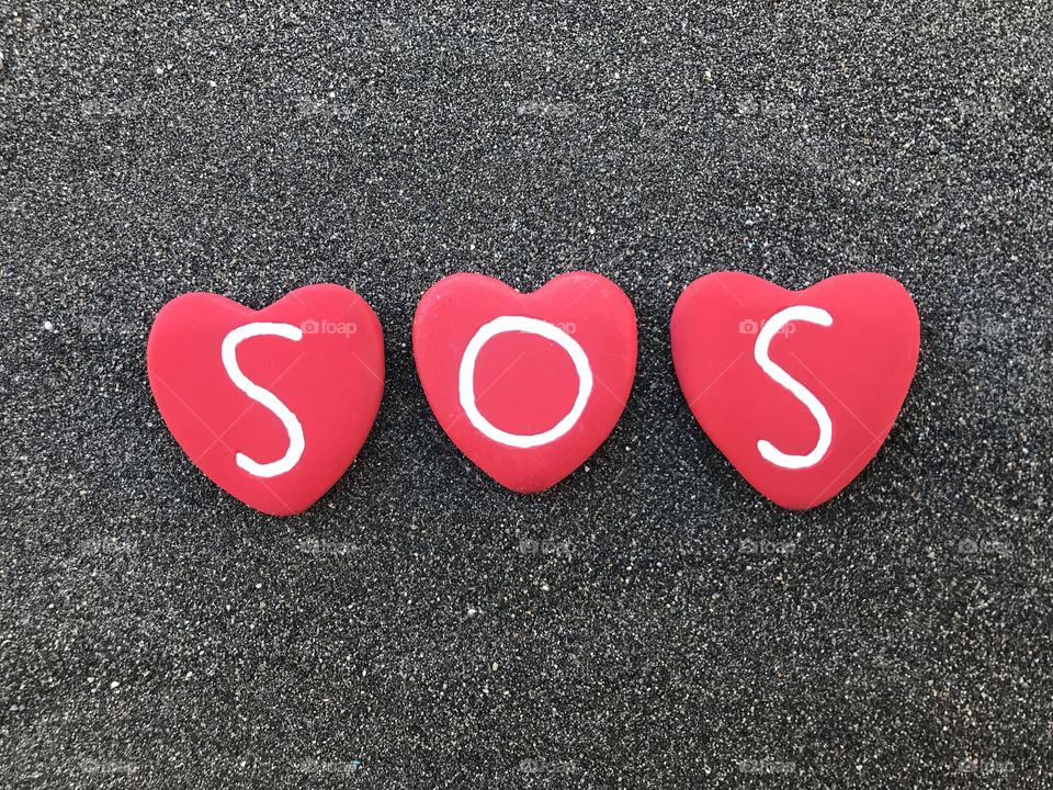 SOS, International Morse code distress signal with colored heart stones over black volcanic sand