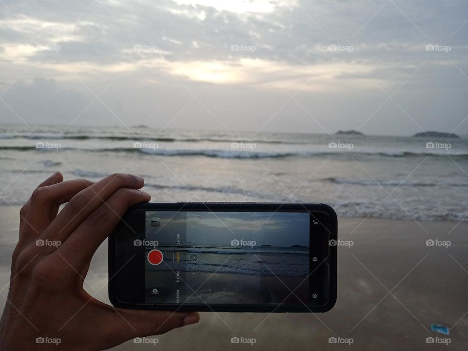 human hand holding mobile phone in beach capchar photo of sunset