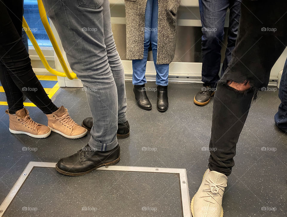 Legs and feet of a group of young people standing on a streetcar all wearing tight jeans and stylish shoes
