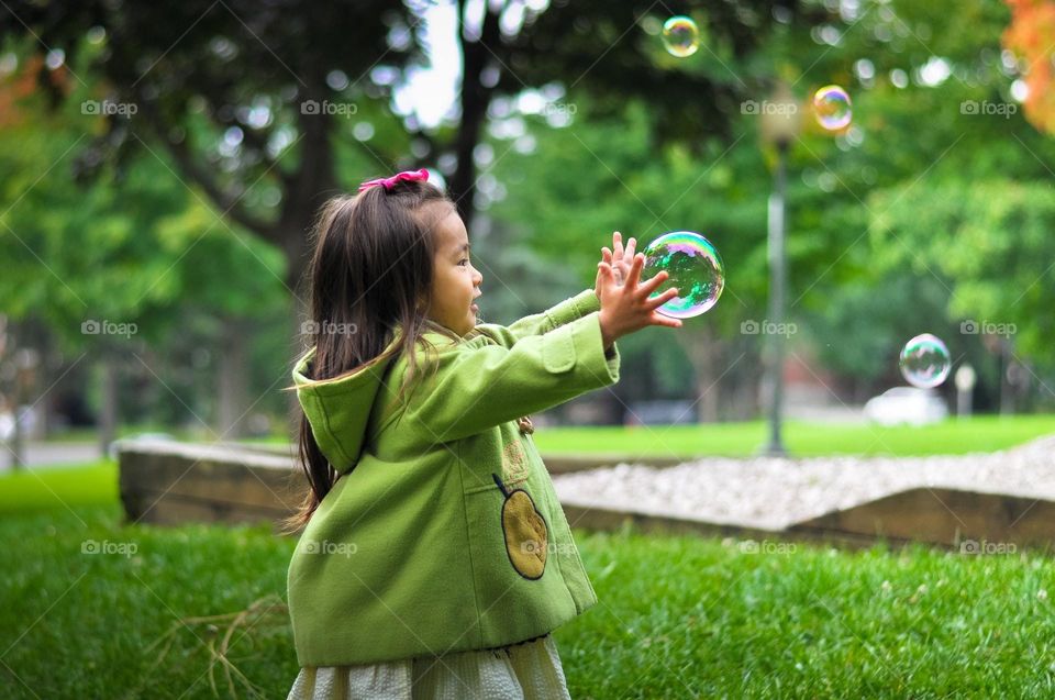 Little girl catching soap bubbles in park