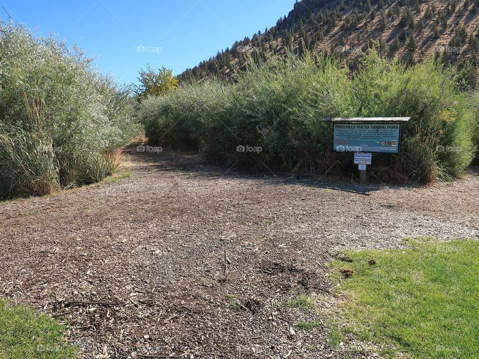 A trail leading to the Prineville Youth Fishing Pond with a sign at Rimrock Park in Prineville on a sunny fall day. 